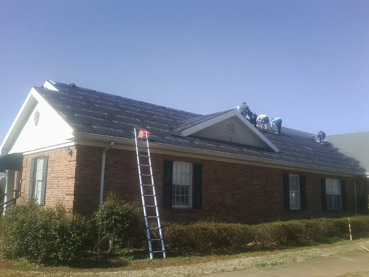 Crew tearing shingles off a brick ranch roof with a ladder set — Metal Roof Repair work by our crew in Pleasant Dale