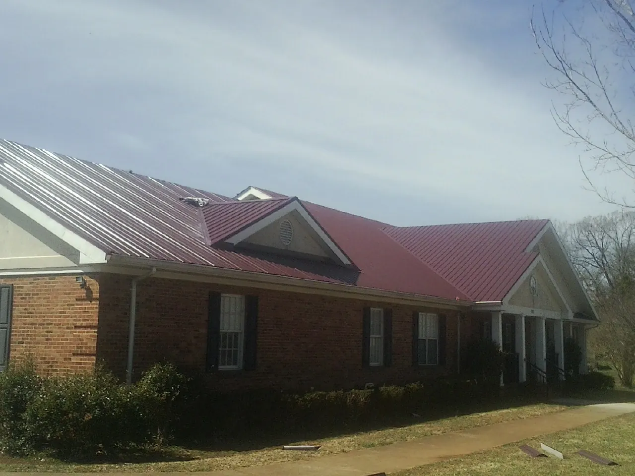 Red metal roof with gabled entries on a long brick building, from a Hail Damage Roof Repair job in Pleasant Dale
