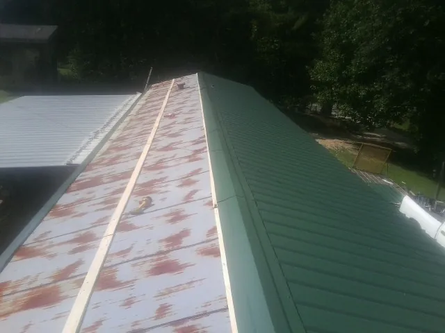 Old rusted panels beside newly installed green metal roofing — Wind Damage Roof Repair by Roofing Brothers in Pleasant Dale