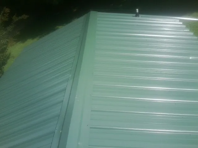 New green metal panels meeting at the ridge of a roof — Flat Roof Repair work by our crew in Pleasant Dale