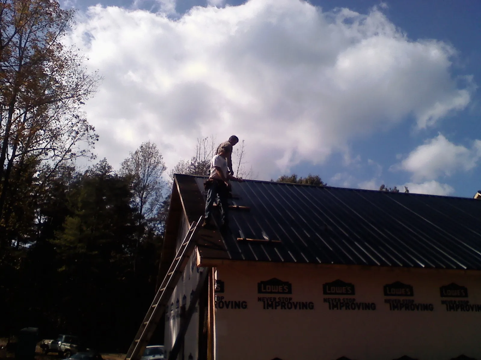 Roofer fastening dark metal panels high against a cloudy sky, from a Roof Inspection job in Pleasant Dale