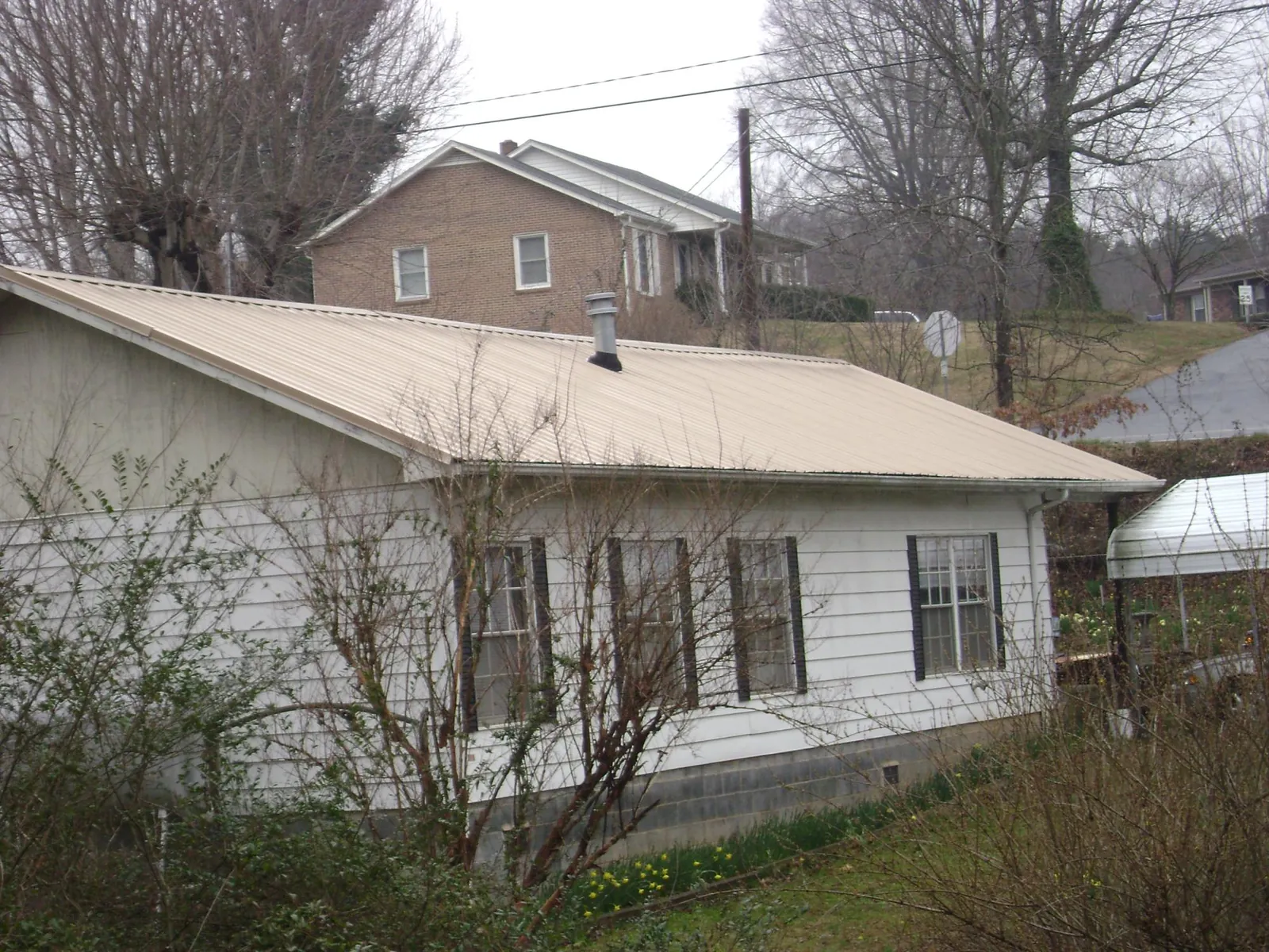 Tan metal roof on a white sided house set into a hillside — Commercial Roofing by Roofing Brothers in Pleasant Dale