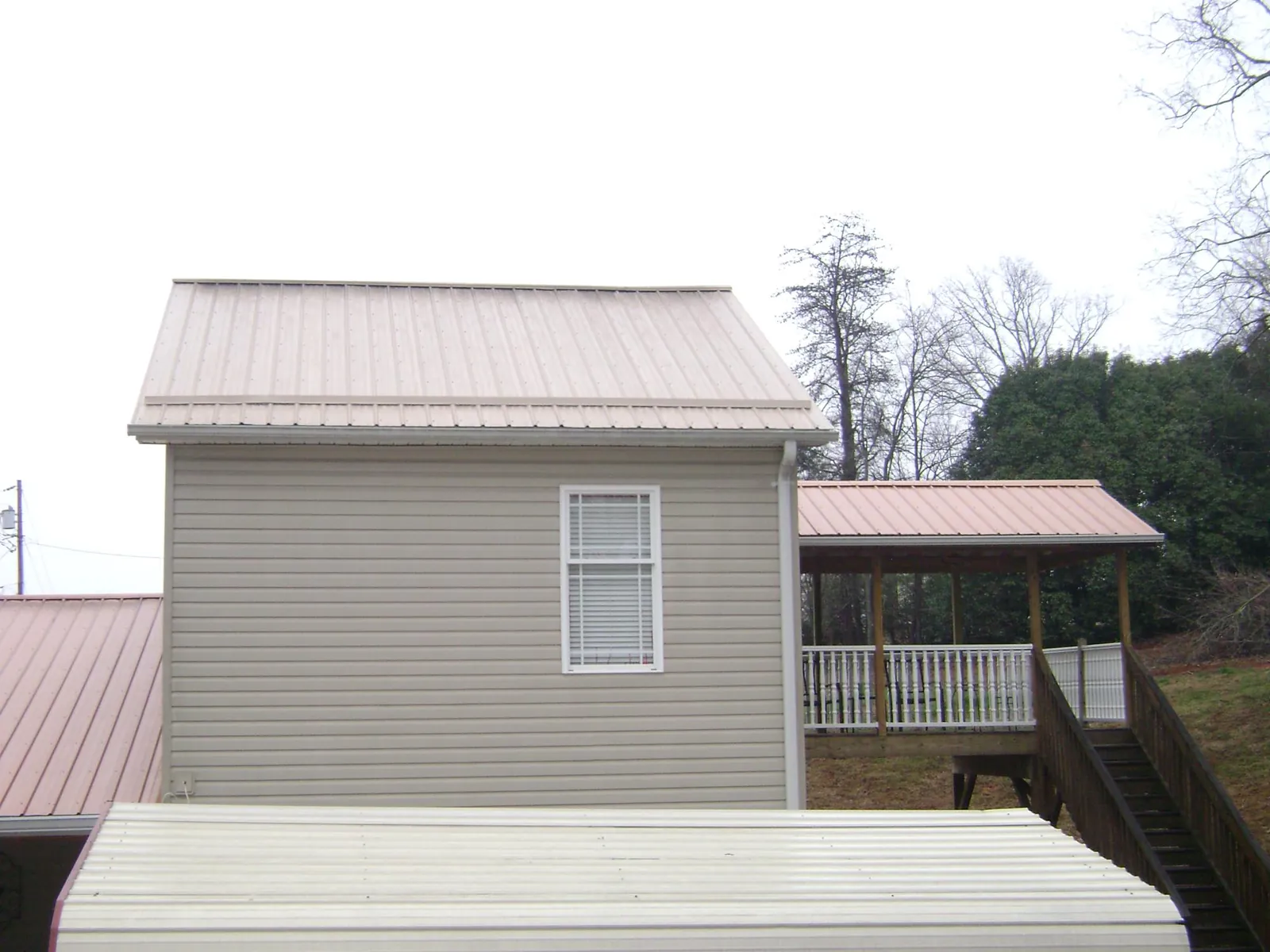 Tan metal roofs on a two story addition and attached porch, from a Roof Replacement job in Pleasant Dale